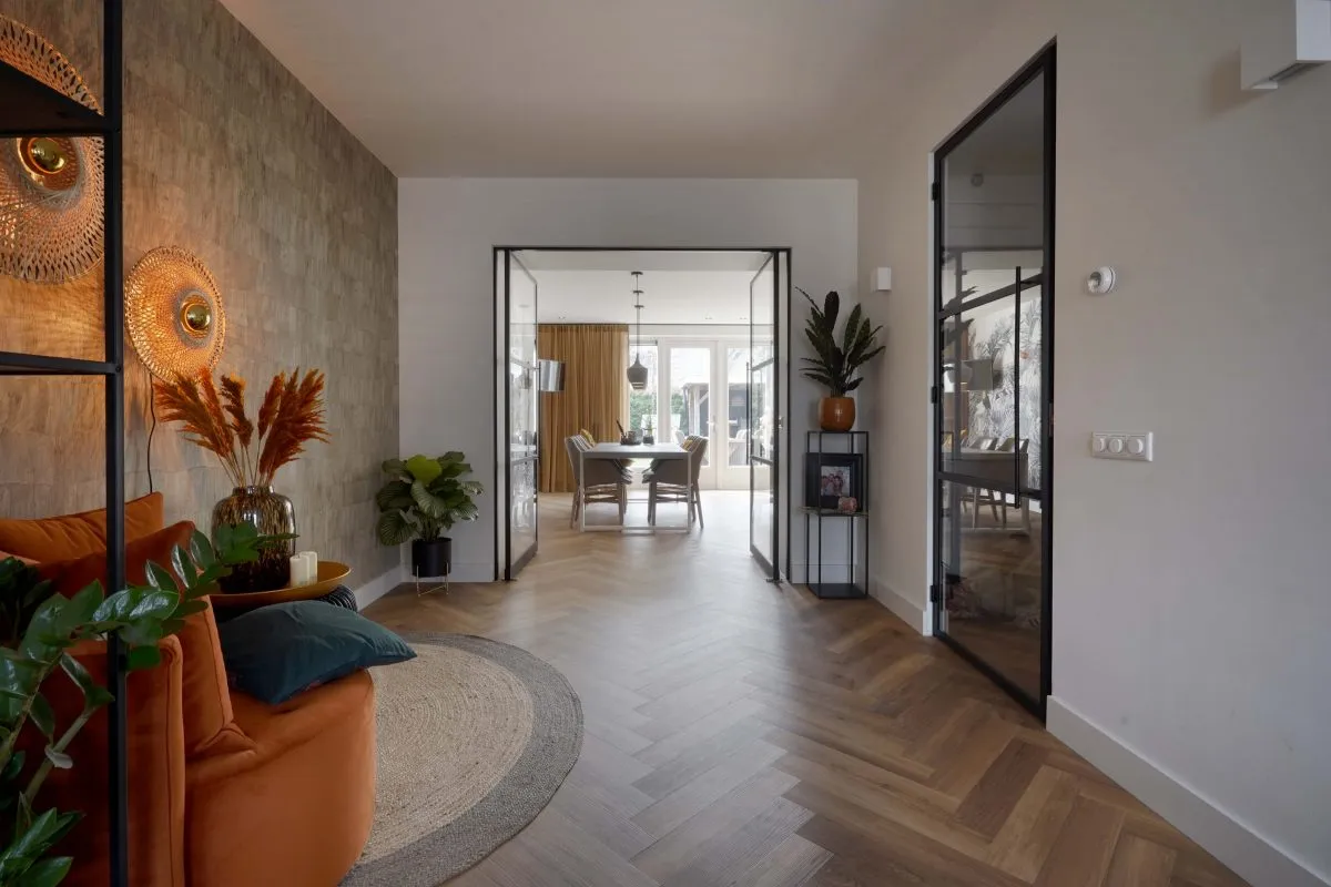 Op de foto zie je een frisse entree die naadloos overloopt in een lichte eetkamer dankzij slanke stalen frames en glazen deuren. Het gaat hier om een interieurinrichtingsdienst waarbij zowel vloer, verlichting als indeling worden vastgelegd en gepresenteerd. Het hoofddoel van deze dienst is het overtuigend in beeld brengen van een woning om potentiële kopers of huurders direct een compleet woonidee te geven. Het visgraatparket oogt duurzaam en heeft een warme houttint die bij elke stijl past, de strakke zwarte deurkozijnen zorgen voor een subtiel industrieel accent en de styling met natuurlijke kleuren en planten laat zien hoe rustige, natuurlijke materialen het wooncomfort verhogen.