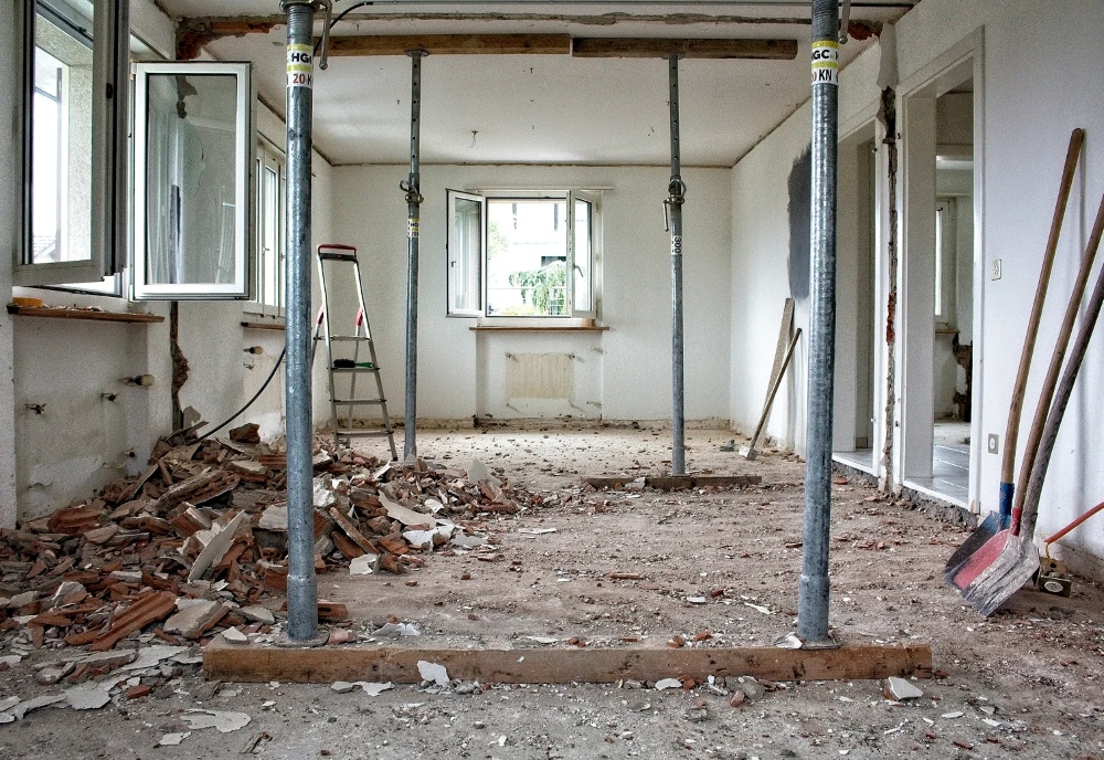 Op de foto zie je een woonruimte waar binnenmuren zijn verwijderd en stalen stempelbalken het plafond tijdelijk dragen. Dit hoort bij een sloop- en renovatiedienst voor interieurtransformatie. Het hoofddoel van deze dienst is om op een veilige manier muren weg te halen en ruimte te creëren voor een nieuwe indeling. Dankzij verstelbare telescopische stutten is er direct hoge draagkracht beschikbaar zonder complexe verankeringswerkzaamheden. Het puin wordt met professioneel materieel afgevoerd om de werkplek schoon te houden. Zo is de volgende bouwfase zonder vertraging te starten.
